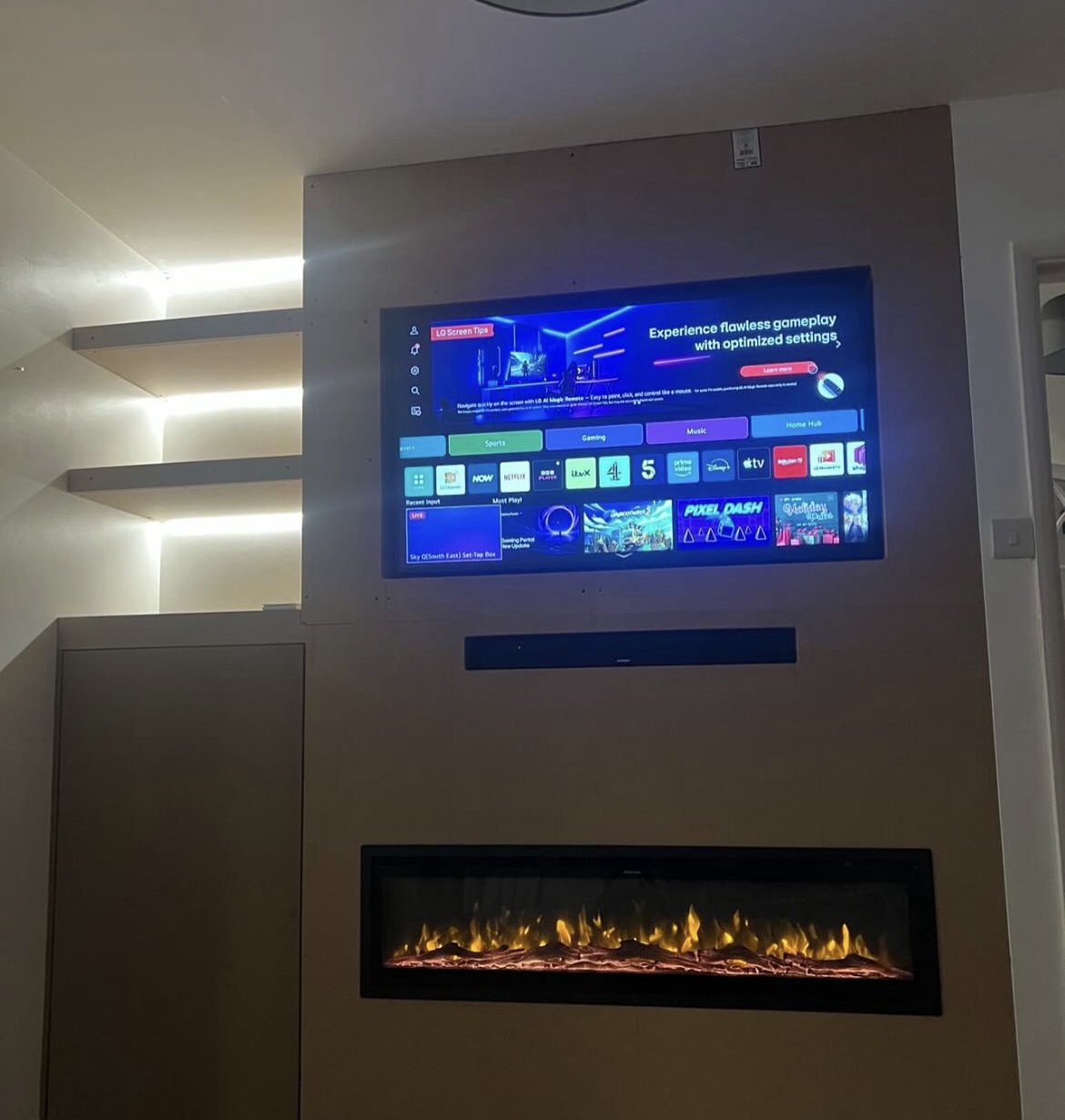 Media wall with inset TV, electric fire, floating shelves and hidden storage cupboard