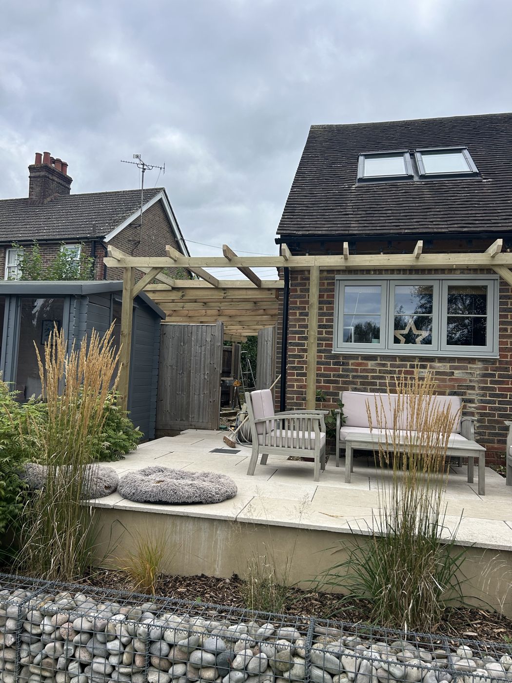 Timber pergola running along the back of a brick house over a patio